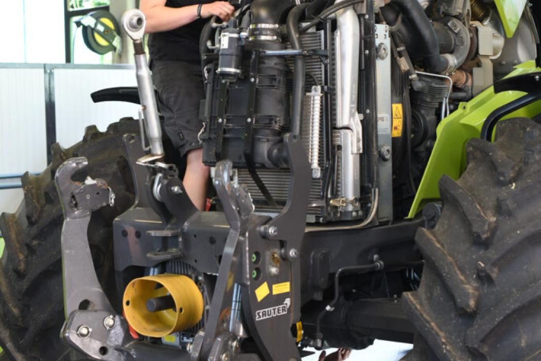 Zwei junge Land- und Baumaschinemechatroniker bei der Arbeit am Motor eines Traktors.