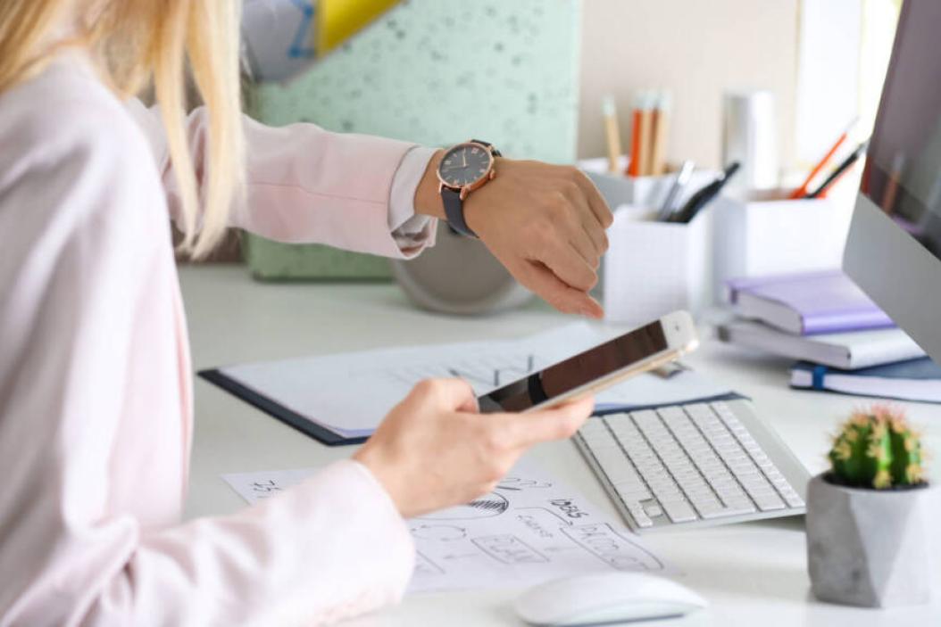 Frau guckt im Büro auf die Uhr - Zeitstress im Arbeitsalltag