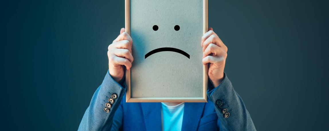 Eine Person hält ein Schild mit einem pessimistischen Smiley-Gesicht vor ihrem Gesicht