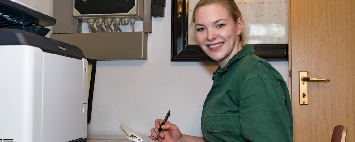 Eine Frau sitzt lächelnd in ihrem Agrarbüro und dokumentiert Daten zur Tierhaltung