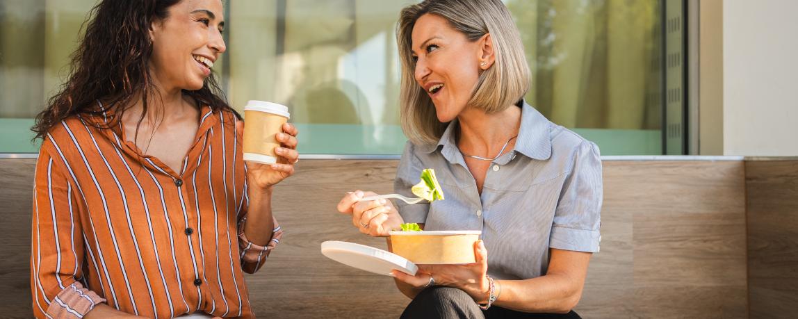 Zwei Geschäftsfrauen beim freundschaftlichen Mittagessen im Freien. Sie essen Salat und trinken Kaffee.