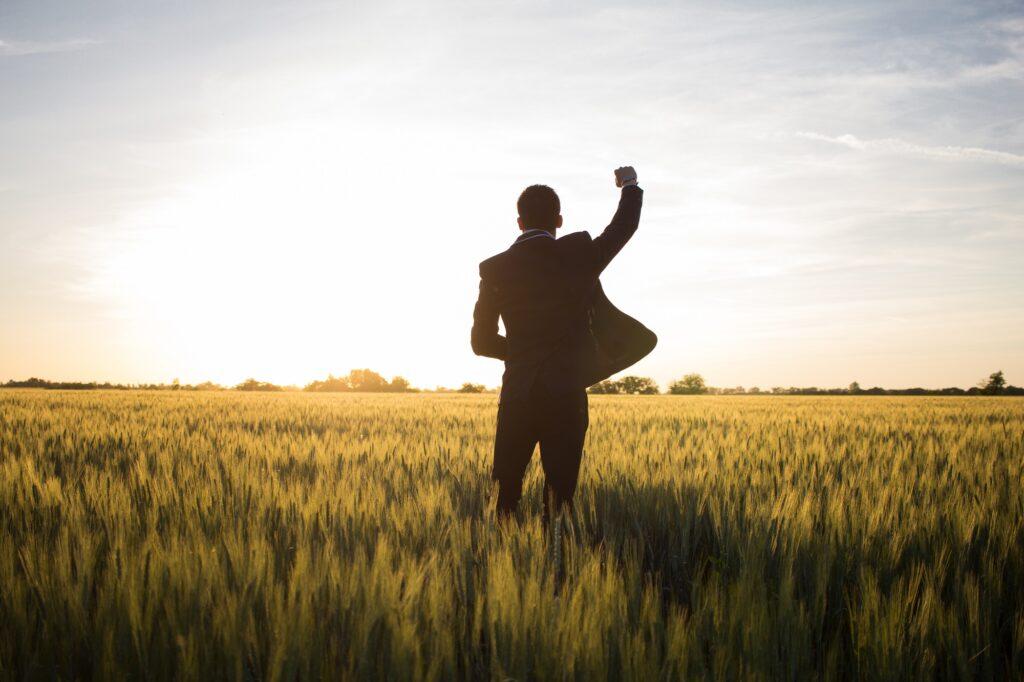 junger Geschäftsmann steht im Feld und freut sich z. Bsp. über eine Beförderung 